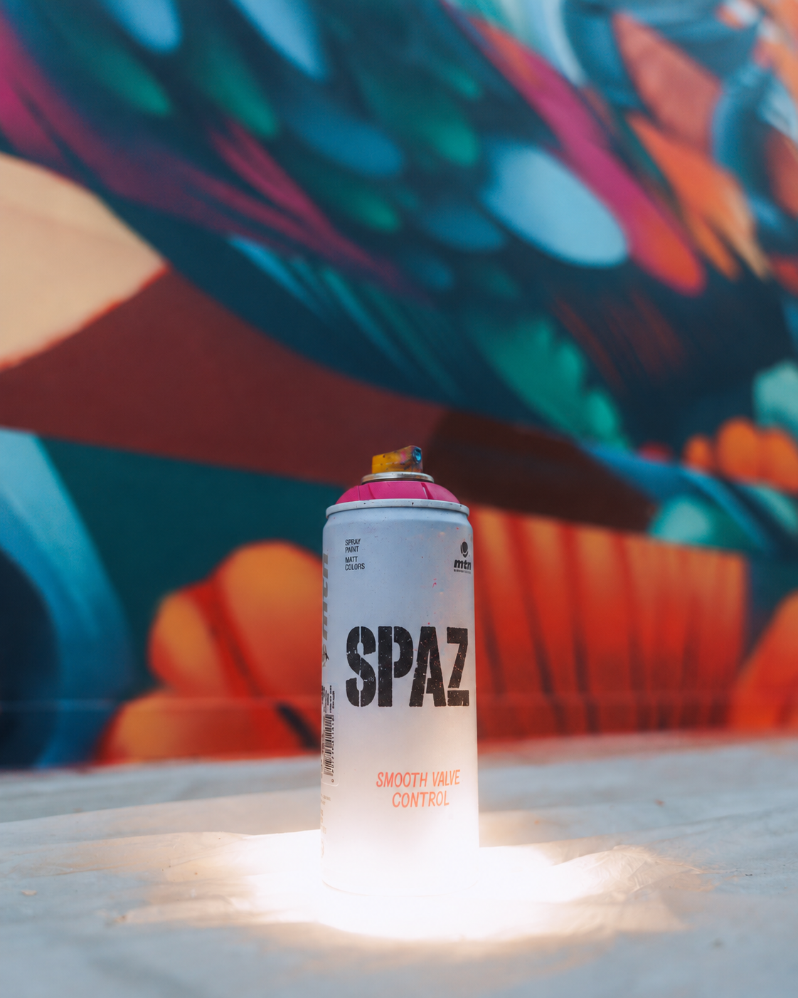 A single spray can marked SPAZ, lit from below in front of the Sikka mural, Dubai, 2025
